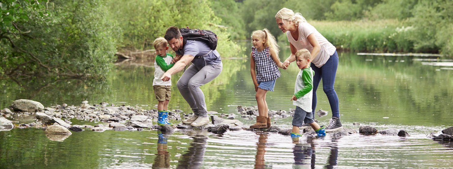 Vater, Mutter und Kinder beim Wandern über einen See.