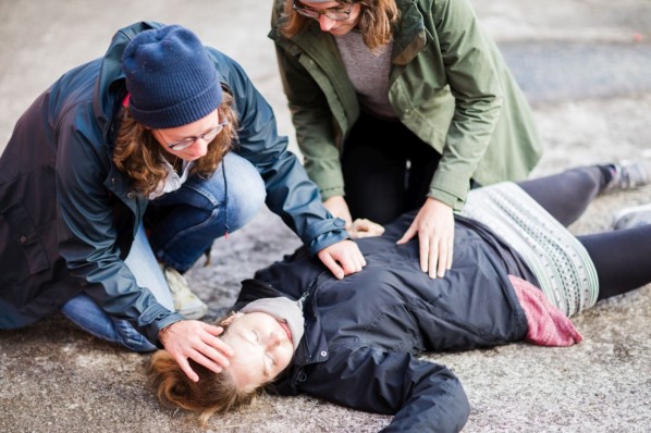 Zwei Frauen Mitte 30 leisten Erste-Hilfe. Die hilfsbedürftige Person liegt auf der Straße.