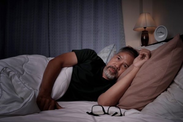 EIne junge Frau recherchiert im Bett liegend auf Ihrem Smartphone nach Ursachsen für Ihre Schlaflähmungen.