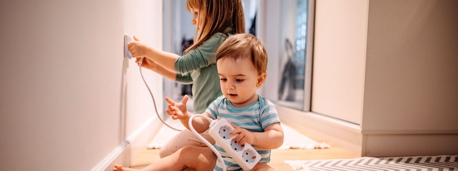 Zwei Kinder spielen in einem Flur an den Steckdosen.