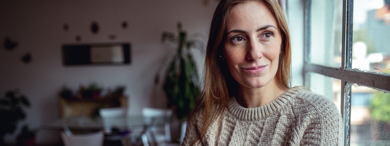 Eine circa 30-jährige Frau schaut schmunzelnd aus dem Fenster.