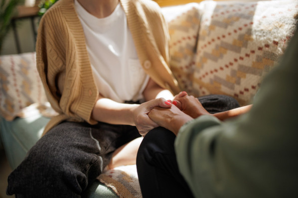 Frauen, die sich auf dem Sofa sitzend die Hände halten und gegenseitig unterstützen
