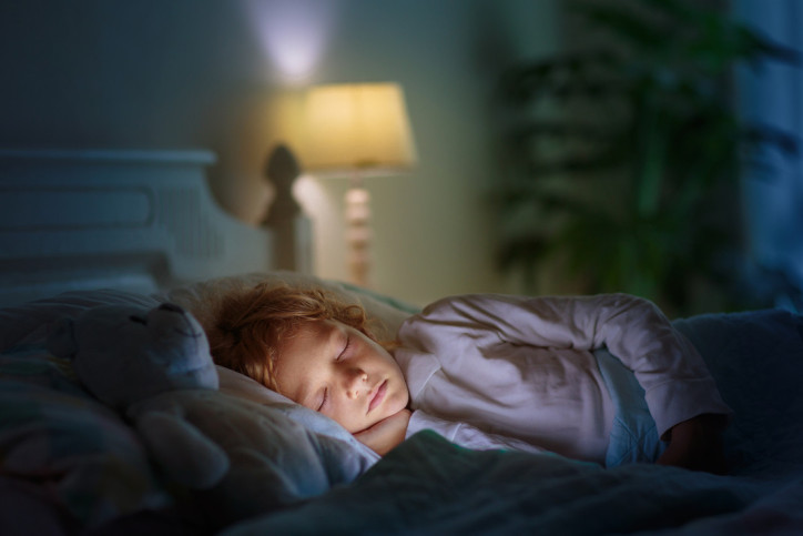 Ein Kind schläft im Bett. Ein kleines Nachtlicht ist im Hintergrund angeschaltet.
