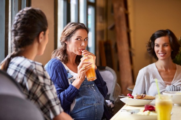 Eine 35-jährige schwangere Frau unterhält sich in einem Café mit ihren beiden Freundinnen.