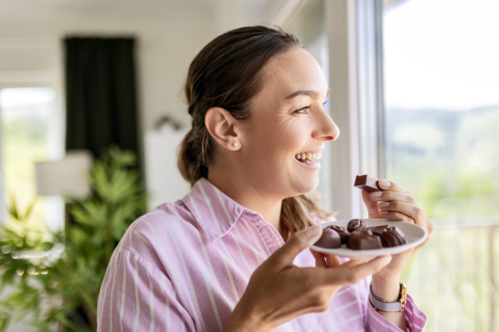 Frau Lächelnd am Fenster Mit Schokolade In Der Hand