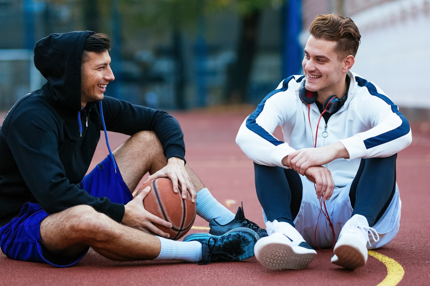 Zwei Basketballspieler sitzen mit Ball auf dem Spielfeld.