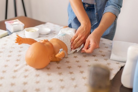 Frau übt an einer Babypuppe Windeln wechseln.