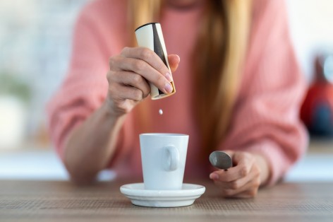 Blonde Frau im rosa Pollover gibt Zuckerersatz n ihren Kaffee