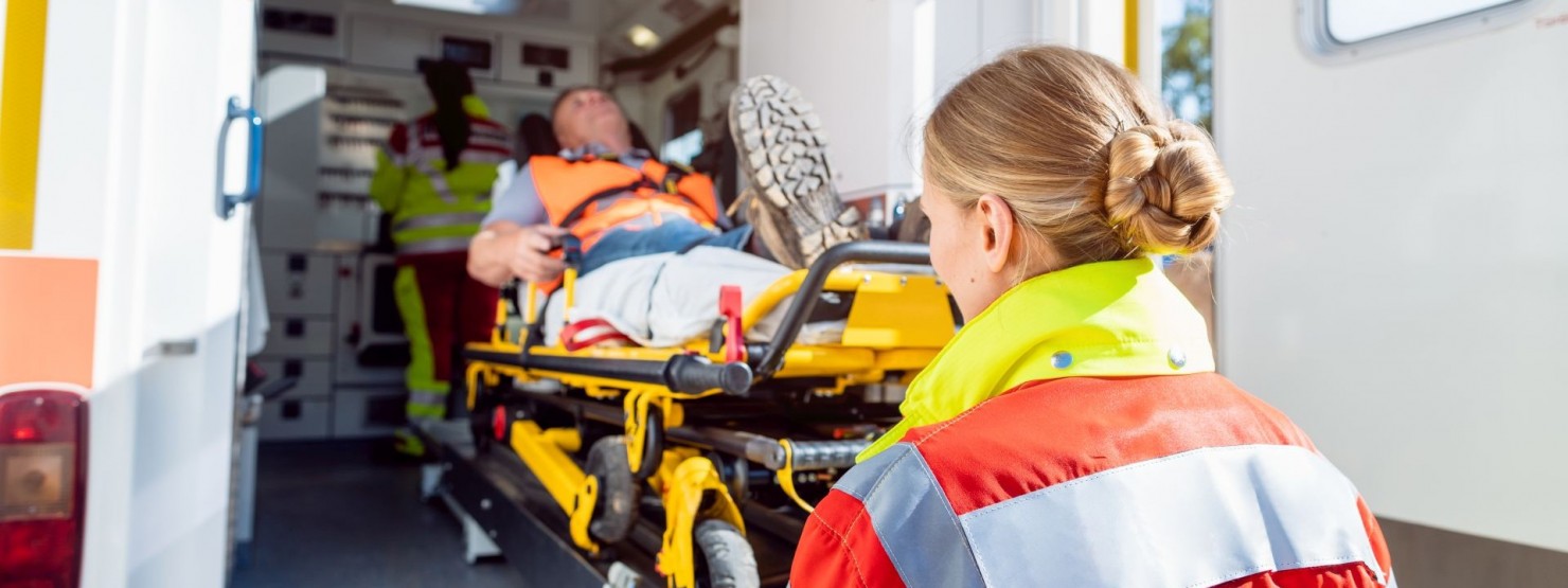 Eine Rettungsassistentin schiebt einen Patienten auf einer Trage in einen Rettungswagen rein.