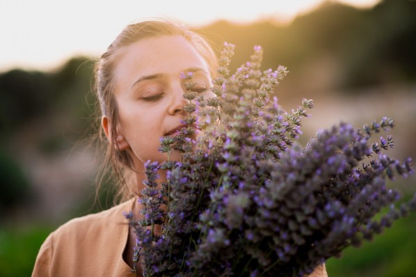 Eine etwa 25-jährige Frau schließt die Augen, während sie an einem Bündel Lavendel riecht.