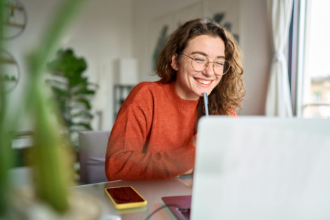 Eine Beschäftigte arbeitet lächelnd im Home Office und nimmt an der Mental Health Week teil.