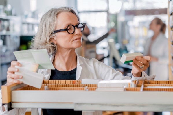 Eine circa 50-jährige Apothekerin sucht ein Medikament aus einem Apothekerschrank heraus. 