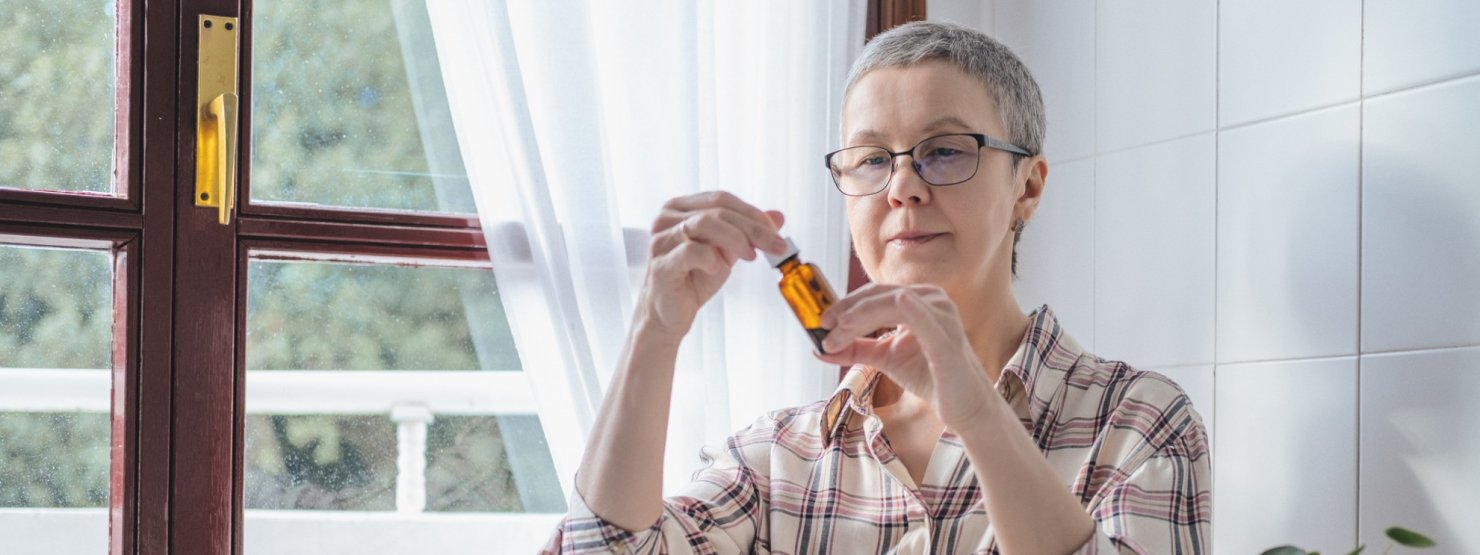 Eine Seniorin in roten Pullover steht in einer Apotheke und lässt sich von einer Apothekerin beraten. Sie lächelt.