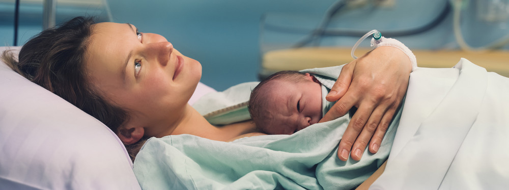 Eine Frau liegt mit ihrem Neugeborenen im Krankenhaus.