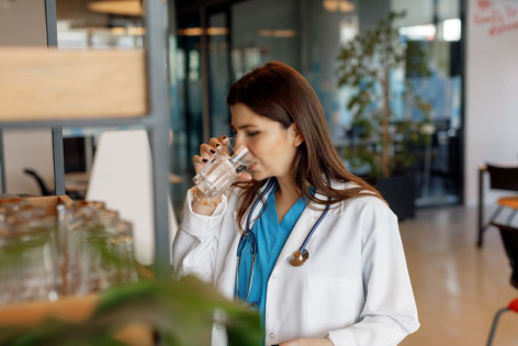 Ärztin trinkt Wasser aus einem Glas, um sich vor Hitze zu wappnen