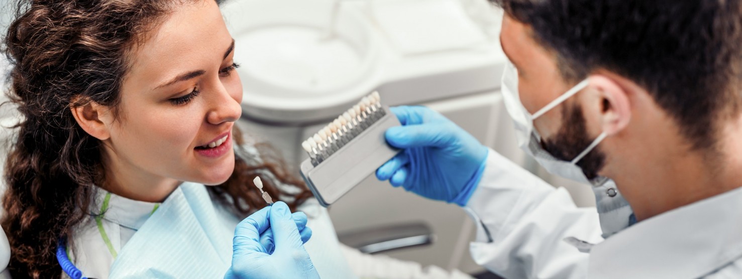 Eine junge brünette Frau sitzt beim Zahnarzt , welche ihr den passenden Zahnersatz zeigt.