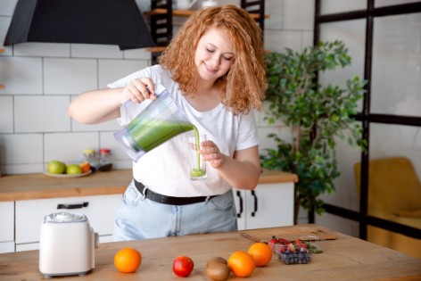 Rothaarige Frau gießt sich einen grünen Saft in ein Glas.