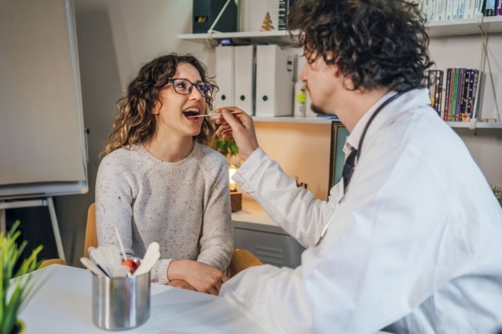 Eine Frau wird von einem Arzt im Mund auf Mundsoor untersucht.