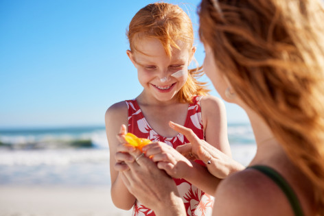 Mutter cremt kleine Tochter am Stand mit Sonnencreme ein