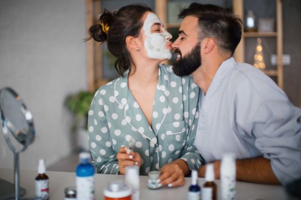 Eine Frau mit frischer Gesichtsmaske küsst ihren Freund auf die Nasenspitze.