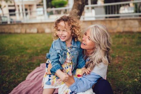 Eine Mutter spielt mit ihrer Tochter zusammen im Garten. Beide lachen ausgiebig.