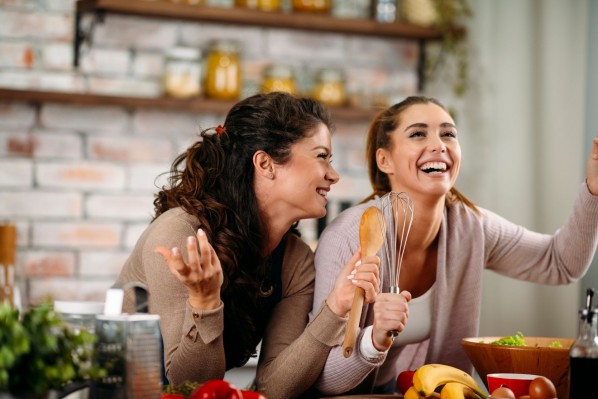 Zwei etwa 20 jährige Frauen stehen gemeinsam in der Küche und kochen. Dabei lachen sie ausgiebig.