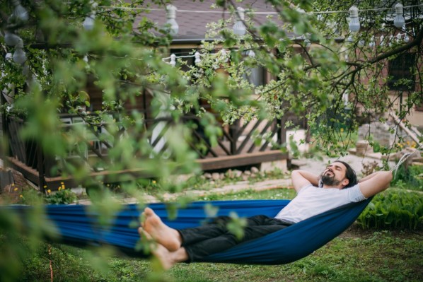 Ein etwa 35 jähriger Mann liegt im Garten in einer Hängematte. Er hat beide Arme hinter dem Kopf verschränkt.