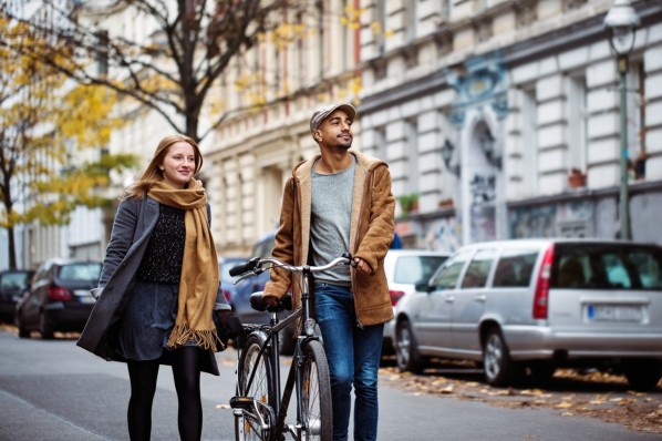 Eine Frau und ein Mann, beide etwa 30 Jahre alt, spazieren durch ein Wohngebiet. Er schiebt ein Fahrrad.