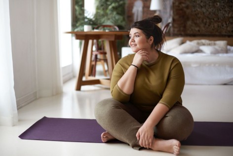 Übergewichtige junge Frau sitzt auf Yogamatte