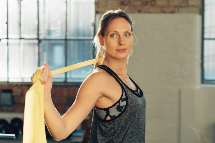 Young woman working out with gym bands or ribbons to stretch and tone her muscles standing in an urban gymnasium with copy space