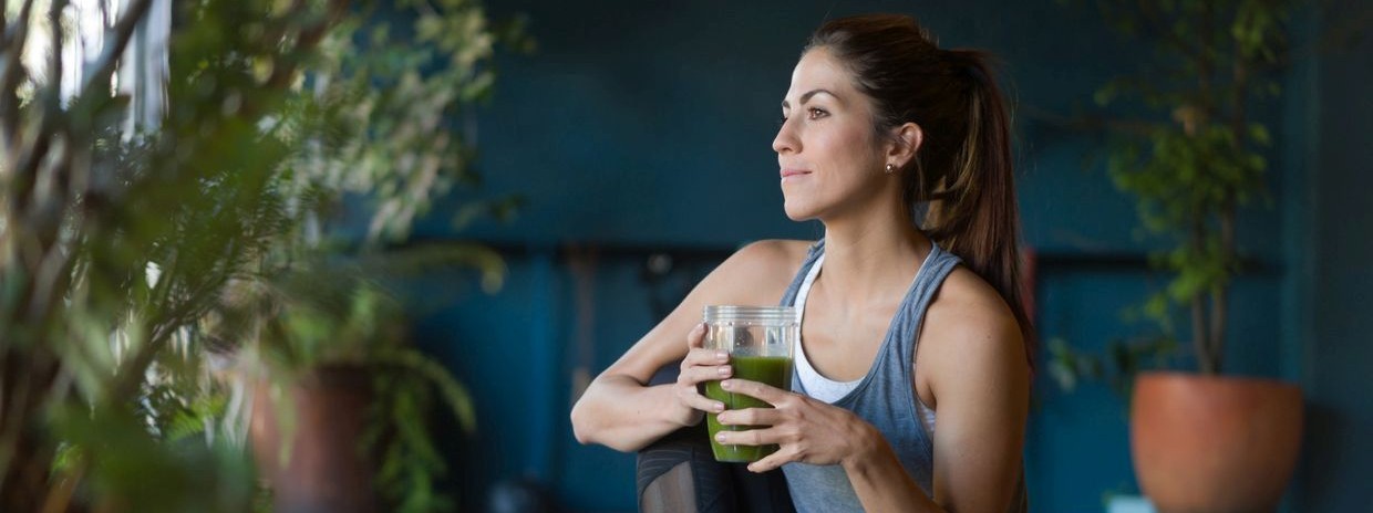 Eine Frau kniet auf ihrer Yogamatte und trinkt einen grünen Smoothie