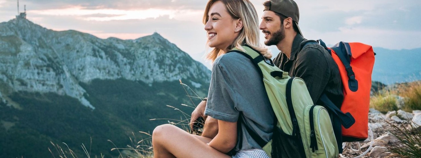 Eine junges Pärchen sitzt auf einem Fels und schaut sich die Berglandschaft an.