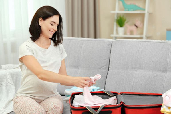 Eine schwangere Frau sitzt auf einem Sofa und packt ihre Kliniktasche für die bevorstehende Geburt.