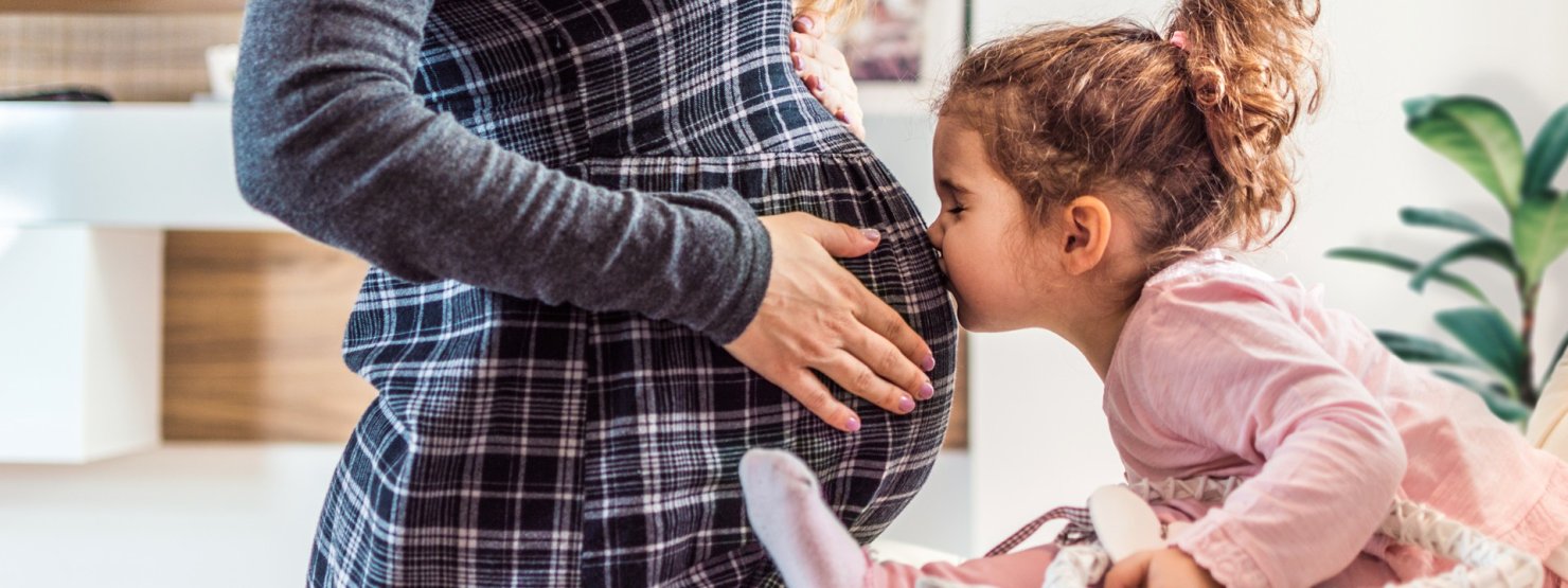 Kleines Mädchen küsst den Babybauch der Mutter