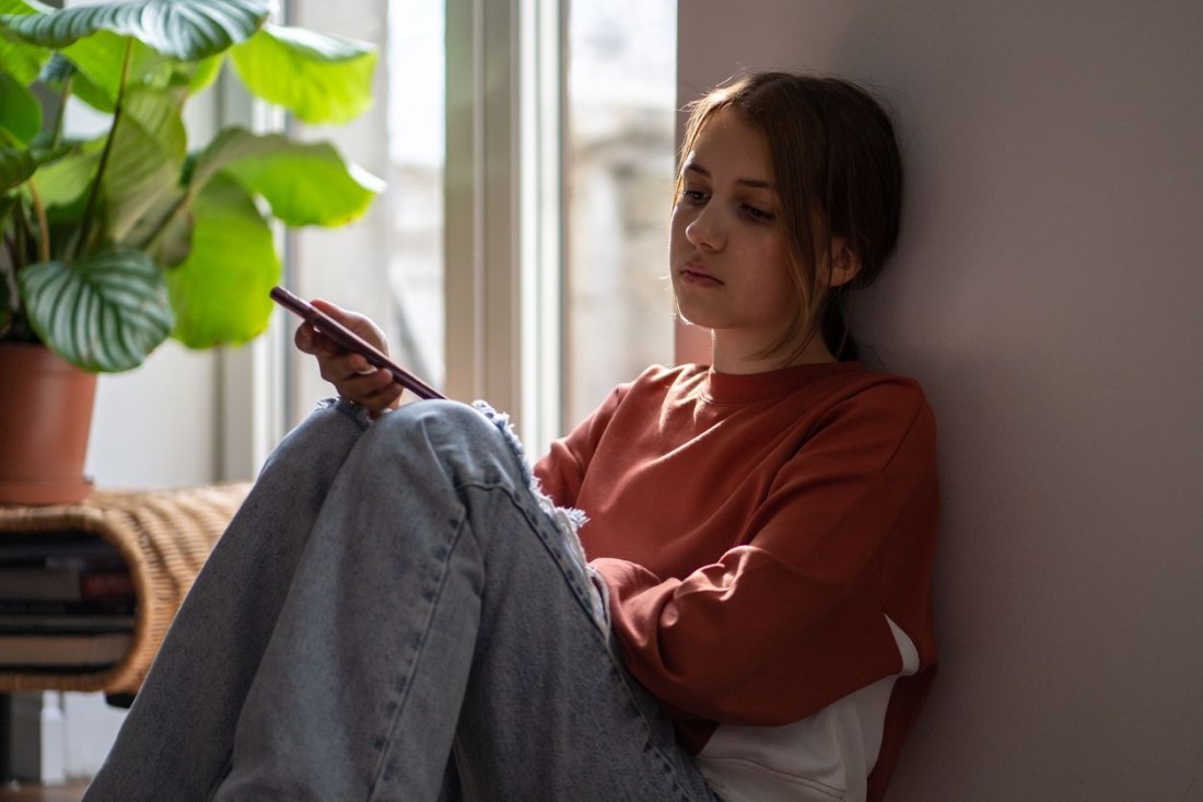 Teenagerin schaut traurig auf ihr Smartphone