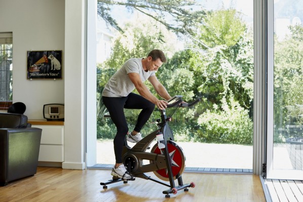 Ein etwa 40 jähriger mann befindet sich im Wohnzimmer auf einem Spinningrad und trainiert.