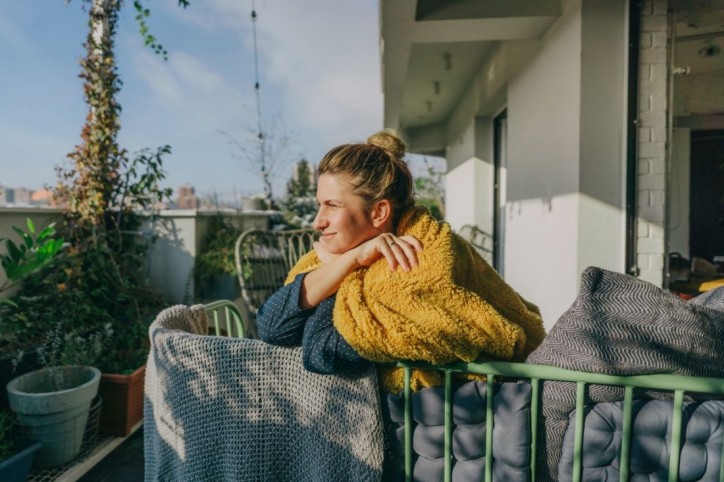 Eine etwa 35-jährige Frau schaut von ihrem balkon aus in die Ferne