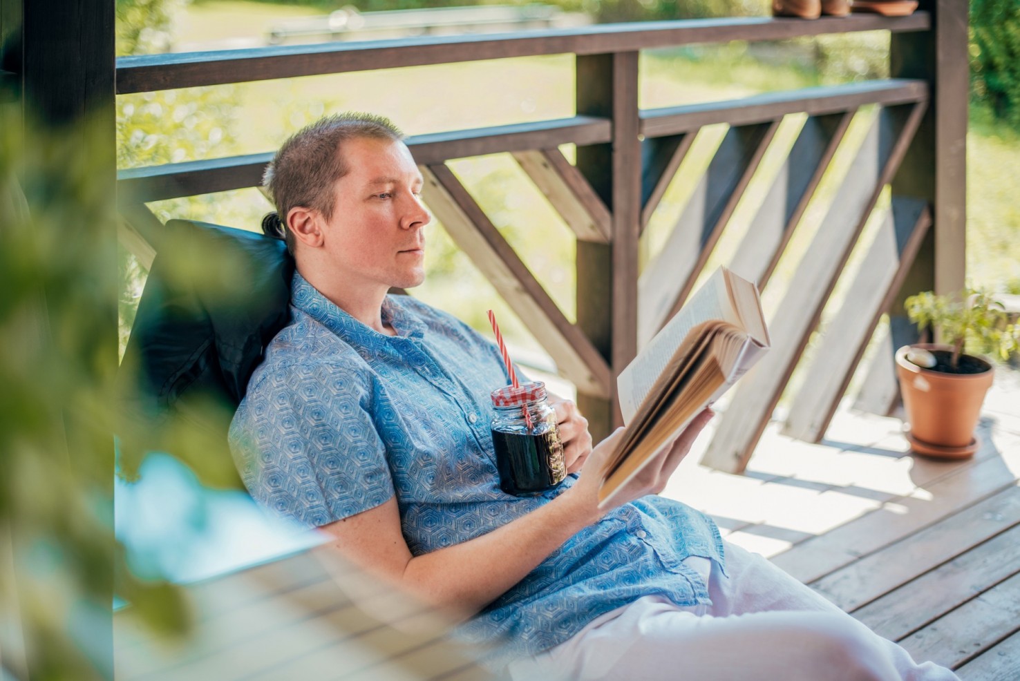 Junger Mann liest im Schatten seiner Veranda ein Buch