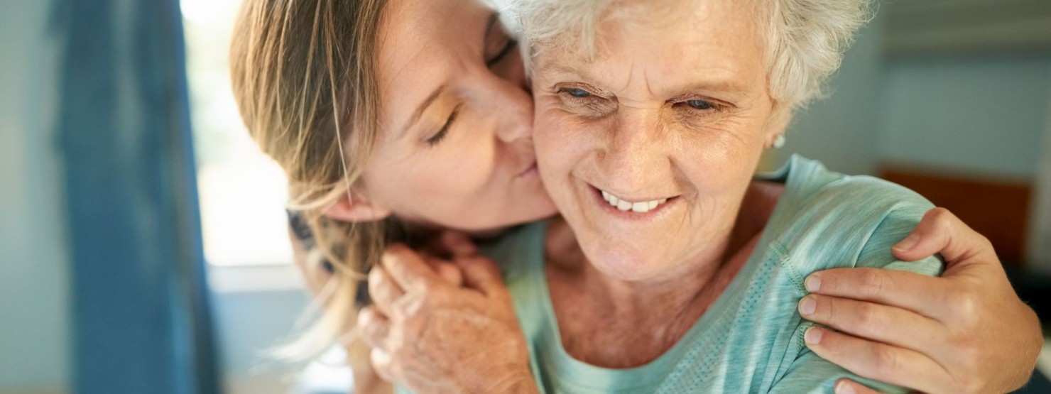 Eine etwa 40-jährige Frau umarmt und küsst eine Seniorin.
