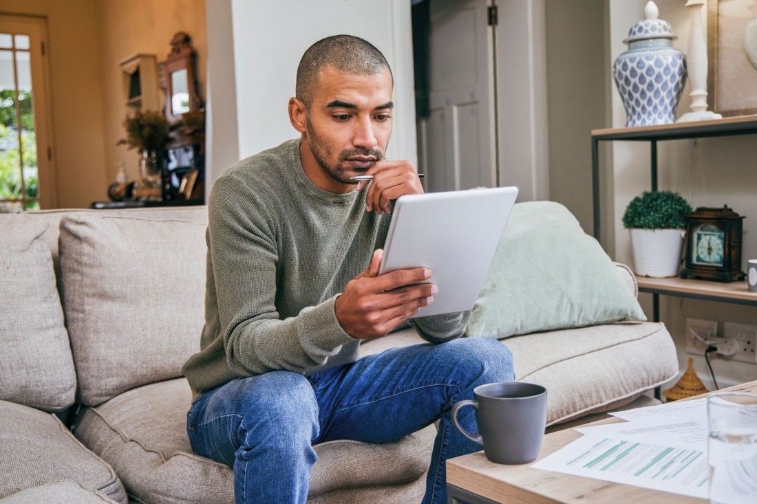 Ein etwa 35 jähriger Mann sitzt auf der Couch und liest interessiert auf seinem Tablet.