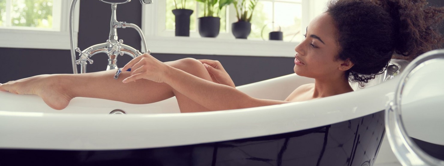 Eine etwa 25 jährige Frau liegt in einer Badewanne und rasiert sich die Beine.
