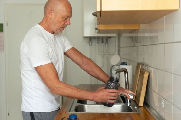 Senior man filling sport water bottle in kitchen.
