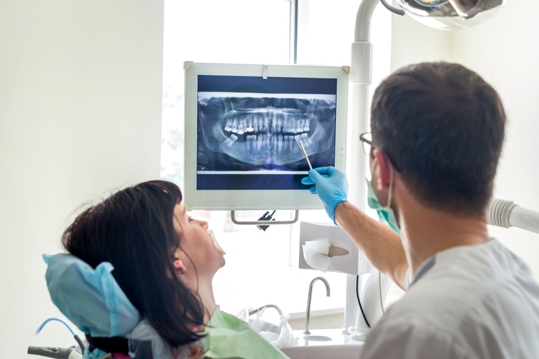 Ein Zahnarzt zeigt seiner Patientin auf einem Röntgenbild ihr Gebiss.