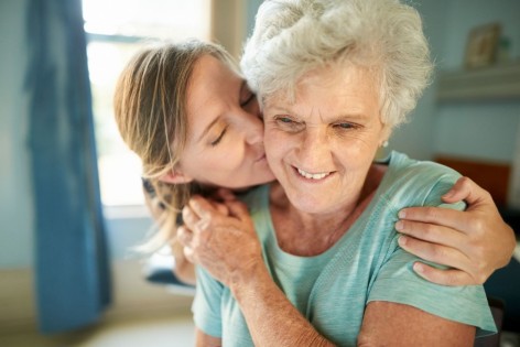 Eine etwa 40-jährige Frau umarmt und küsst eine Seniorin.