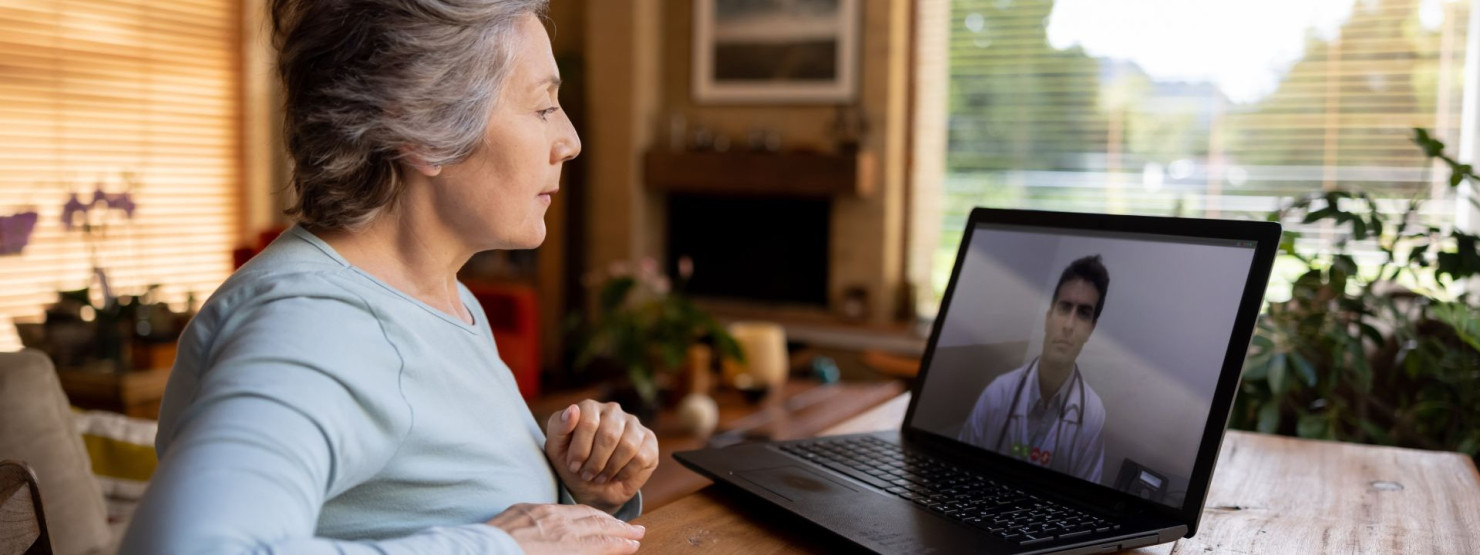 Eine etwa 60-jährige Frau sitzt am Tisch, schaut auf ihren Laptop und hört einem Arzt vom Unimedizin Halle-Talk zu.