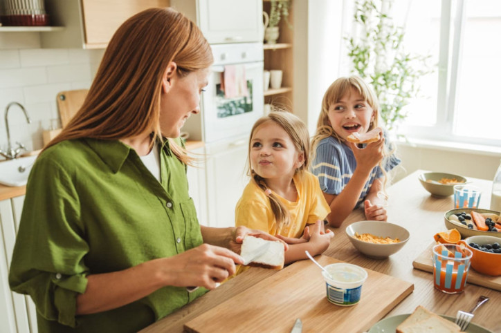 Ein glückliche Mutter bereitet ihren kleinen Töchtern Essen zu.