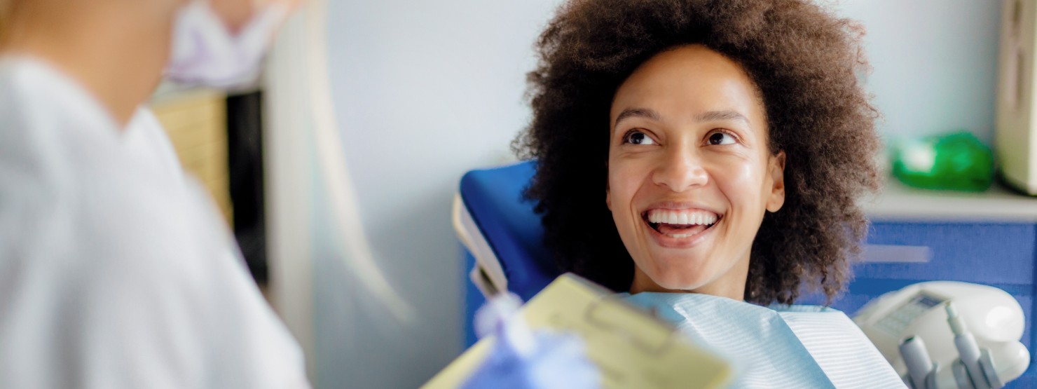 Eine etwa 35-jährige Frau sitzt auf einem Zahnarztstuhl und lächelt ihre Ärztin an.