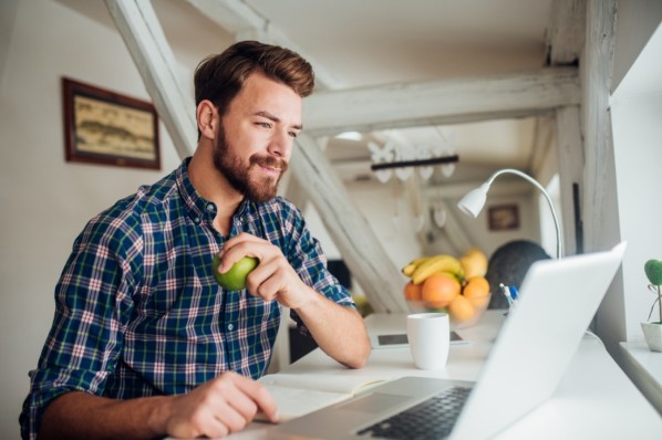 Smiling man healthy eating when using laptop at home