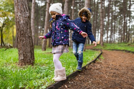 Ein etwa 4 jähriges Mädchen und ein 4-jähriger Junge balancieren auf einer Bordsteinkante im Park