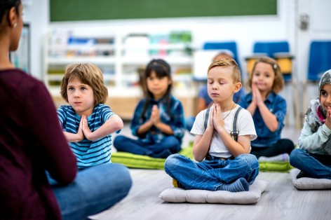 Kinder sitzen im Schneidersitz auf Matten und meditieren.